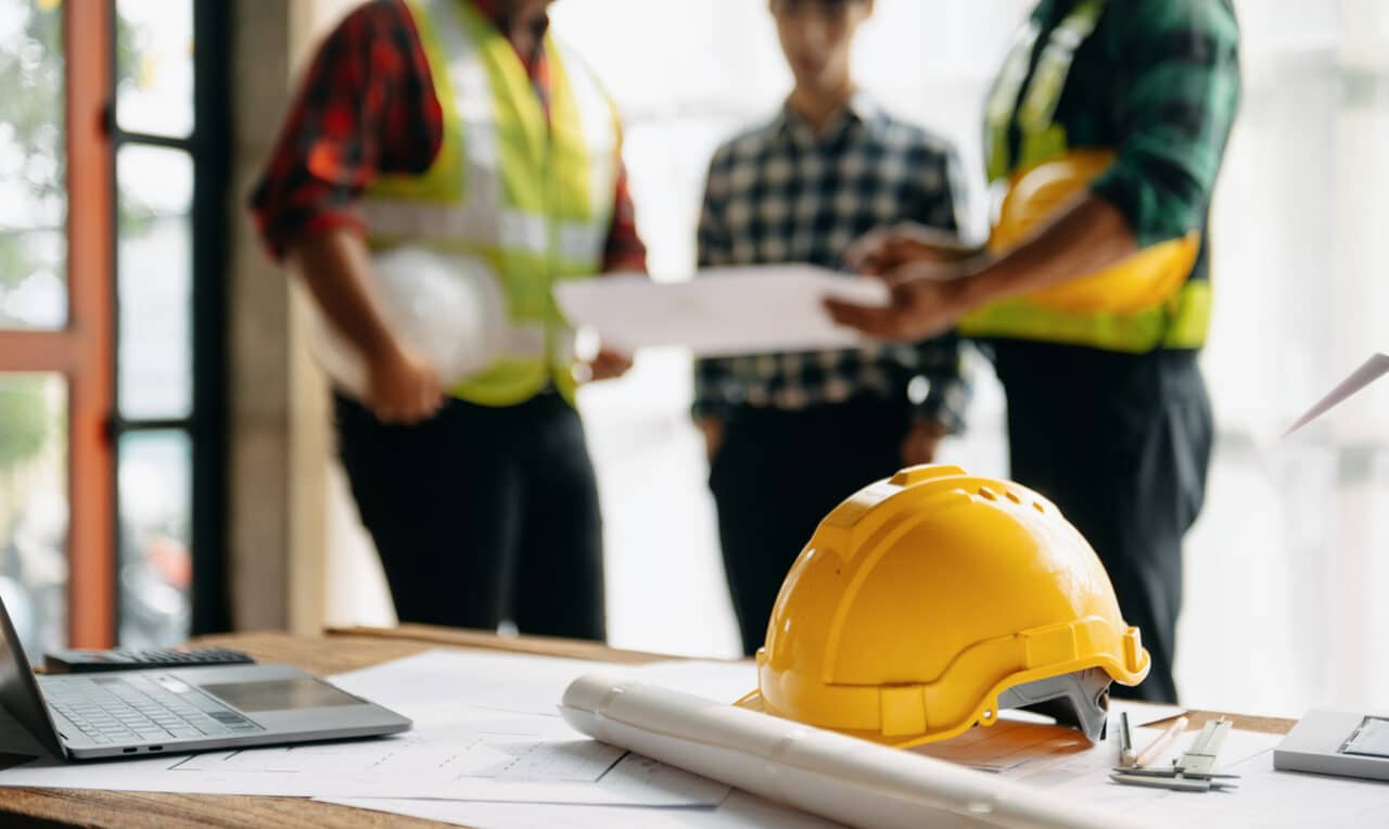 Construction site workers looking at plans. Hardhat on a table.