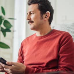 Happy man wearing hearing aids holding a smartphone