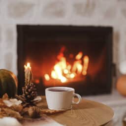Warm cup of tea, pumpkin, autumn leaves on wooden table on background of burning fireplace