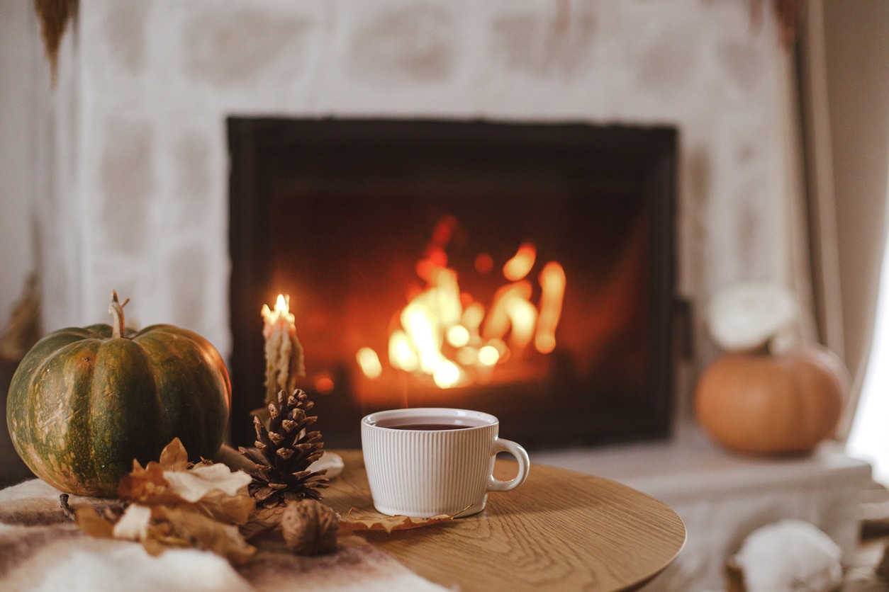 Warm cup of tea, pumpkin, autumn leaves on wooden table on background of burning fireplace.
