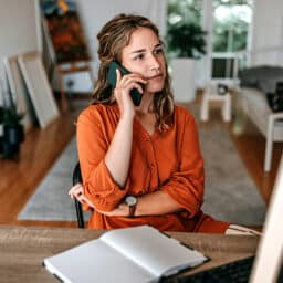Young woman talking on smart phone while working at home office