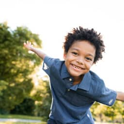 Smiling boy in the park holding his arms out wide.