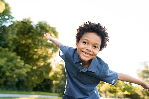 Smiling boy in the park holding his arms out wide.
