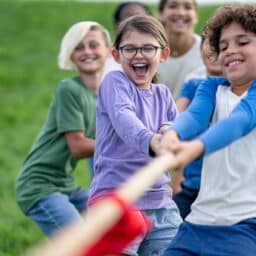 A small group of school aged children pull a rope with all their might, as they participate in a game of tug-of-war.