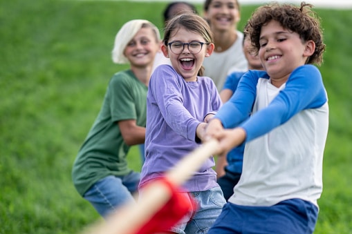 A small group of school aged children pull a rope with all their might, as they participate in a game of tug-of-war.