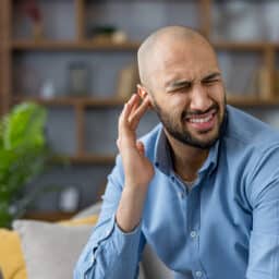 Man with tinnitus touching his ear and frowning.