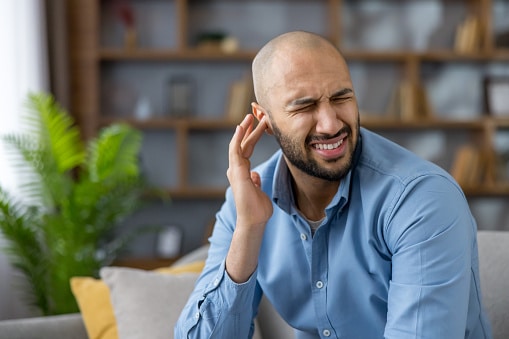 Man with tinnitus touching his ear and frowning.